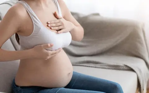 Kobieta w ciąży, dotykająca swoich piersi. Zmiany w sutkach w ciąży to naturalny proces.
