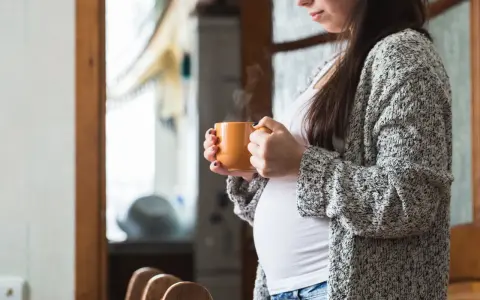 Ciepły napar z rooibos w dłoniach ciężarnej kobiety. Delikatny dym unosi się z kubka, tworząc chwilę spokoju.