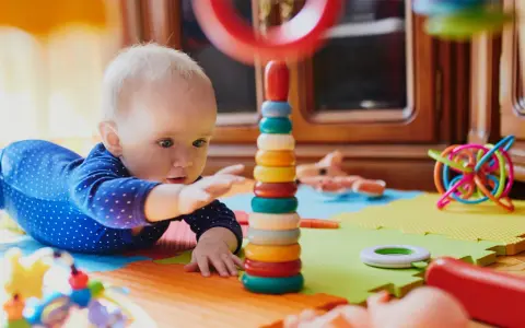 Zaintrygowany 6 miesięczne dziecko próbuje sięgnąć kolorowych kółek wieży.