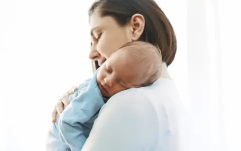 Matka tuląca śpiącego niemowlaka na ramieniu.