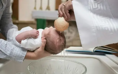 Chrzestna polewa główkę dziecka wodą święconą z muszli podczas ceremonii chrztu.