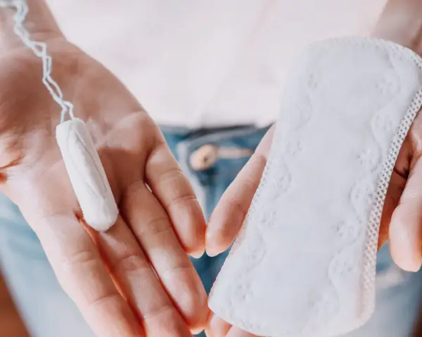 Dłonie trzymają tampon i podpaskę. Czasem pojawia się plamienie zamiast okresu, wtedy wybór jest ważny.