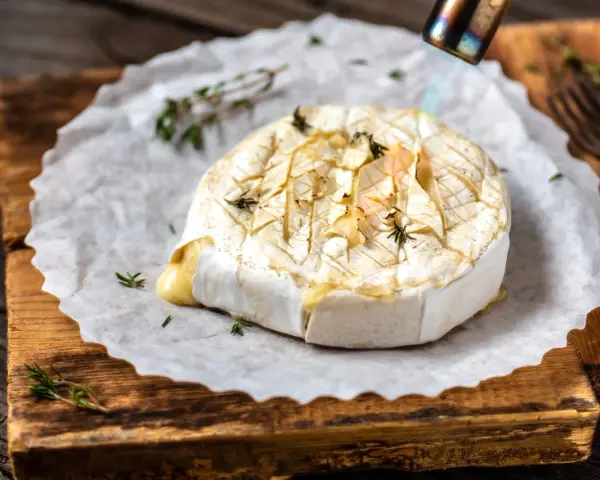 Topiony camembert w ciąży, zapiekany palnikiem z ziołami, na desce.