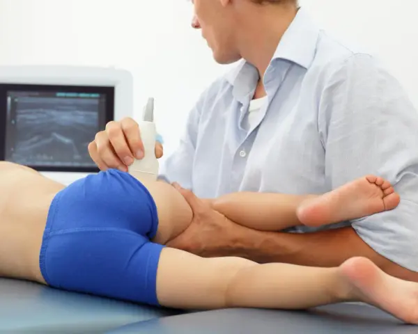 Lekarz wykonuje USG bioder u dziecka, diagnozując zapalenie stawu biodrowego.