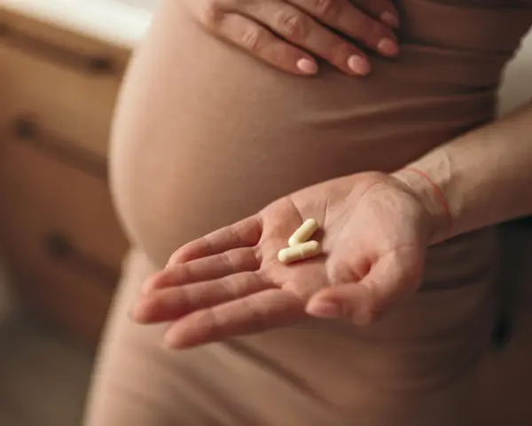 Dłoń kobiety w ciąży trzyma dwie kapsułki. Ostrożność przy wyborze antybiotyku w ciąży jest kluczowa dla zdrowia matki i dziecka.
