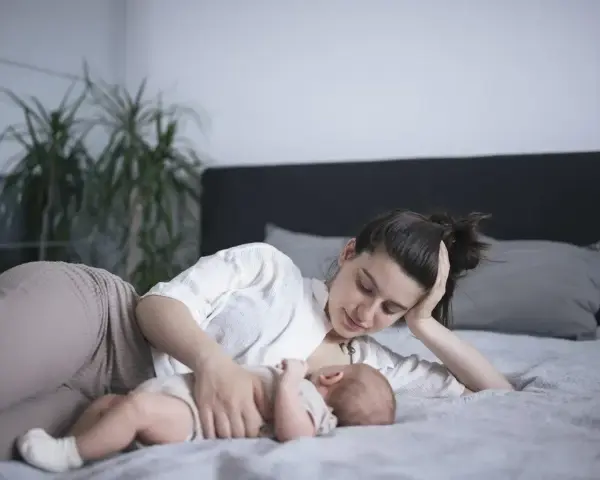 Matka karmi piersią dziecko na leżąco, opierając głowę na dłoni. Czuły moment bliskości.