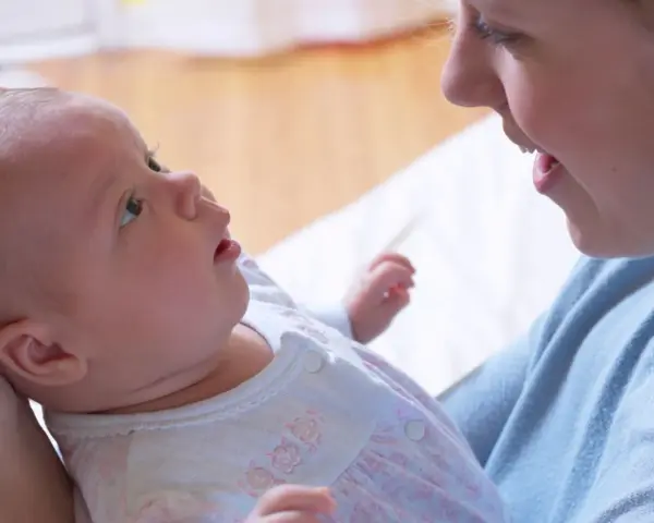 Uśmiechnięta mama patrzy na swoje 6 tygodniowe dziecko, które z zaciekawieniem spogląda w górę.