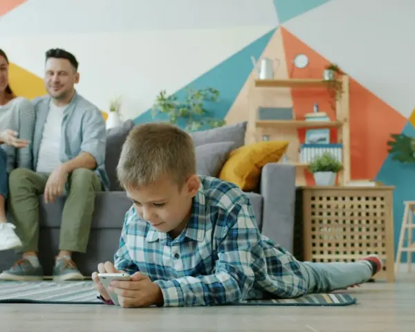 Chłopiec gra na telefonie, podczas gdy rodzice siedzą na kanapie. Ciekawe, od ilu lat jest WhatsApp i czy oni też go używają?
