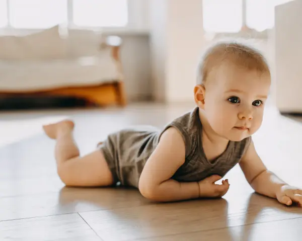 Dziecko w body leży na brzuchu na drewnianej podłodze, patrząc w bok.