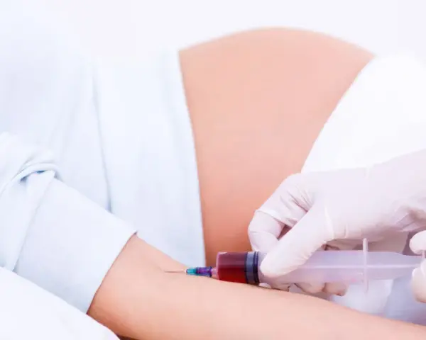 Pobieranie krwi do badań w 15 tygodniu ciąży. Brzuch ciężarnej i ręka z igłą strzykawki.