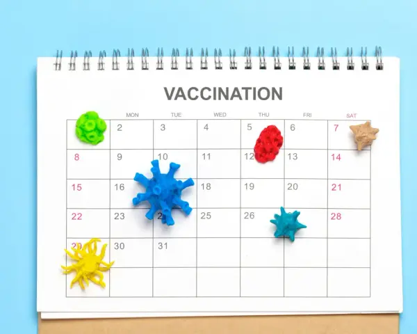 Kalendarz z napisem "VACCINATION" i kolorowymi modelami wirusów na dniach. Planowanie szczepień to klucz do pokonania pandemii.