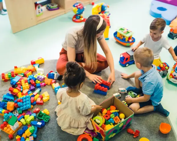 Dzieci bawią się klockami z opiekunką, co może być możliwe dzięki dofinansowaniu do żłobka. Radość i nauka przez zabawę.