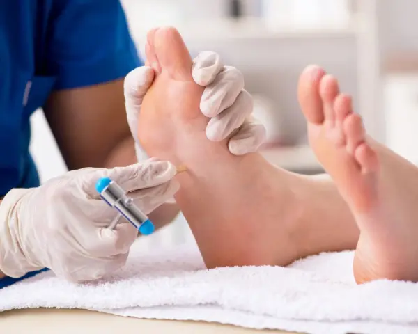 Lekarz w rękawiczkach bada stopę pacjenta młoteczkiem neurologicznym.