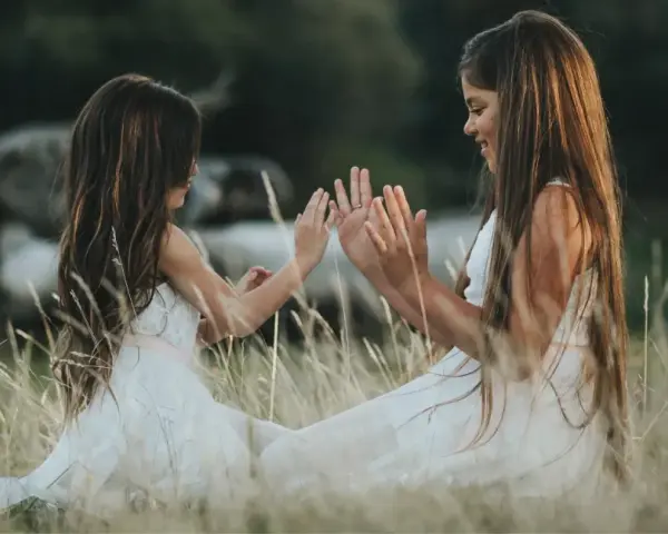 Dwie dziewczynki w białych sukienkach siedzą na łące i bawią się w "pajacyka". To idealna wyliczanka dla dzieci, która rozwija koordynację ruchową.
