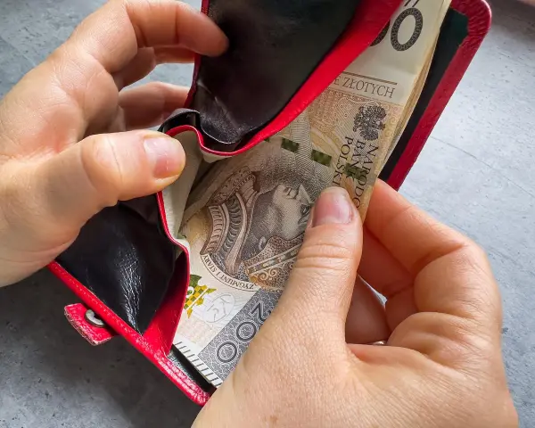 Ręce wkładają banknoty do czerwonego portfela. To może być 1000 zł na drugie dziecko, wsparcie dla rodziny.