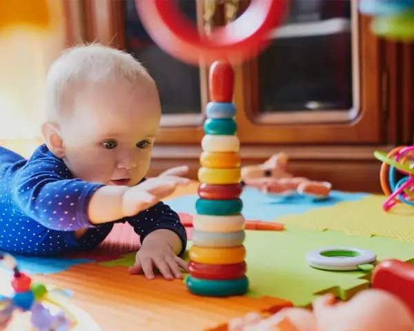 Zaintrygowany 6 miesięczne dziecko próbuje sięgnąć kolorowych kółek wieży.