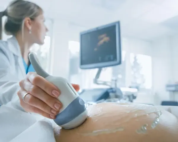 Lekarka wykonuje USG brzucha ciężarnej, monitorując przebieg ciąży. Badanie to jest kluczowe, zwłaszcza gdy stosowana jest heparyna w ciąży.