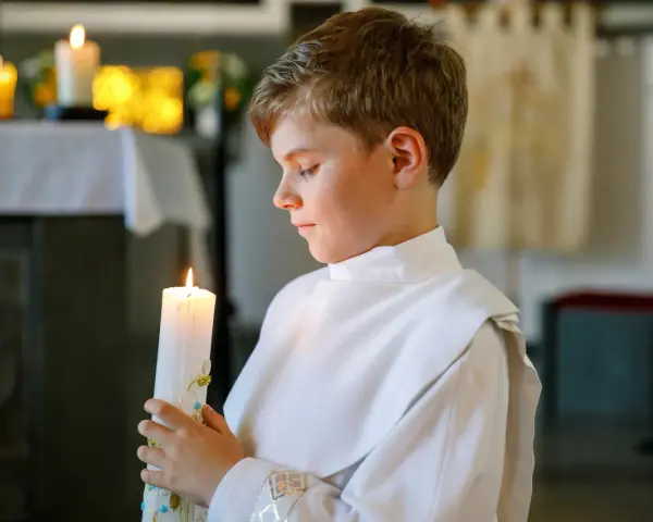 Chłopiec w białej szacie trzyma zapaloną świecę. To ważny moment, jak zorganizować chrzciny, by był niezapomniany.
