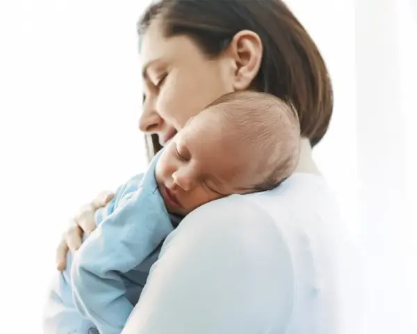 Matka tuląca śpiącego niemowlaka na ramieniu.
