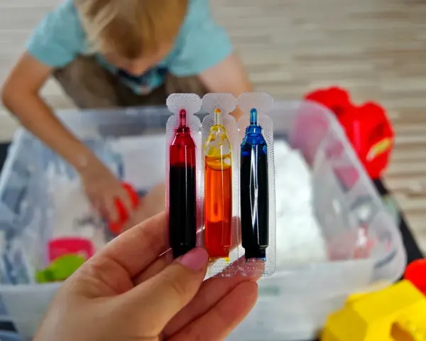 Kolorowe barwniki do piankoliny, idealne do domowego przepisu na kreatywną zabawę. Dziecko w tle miesza składniki.