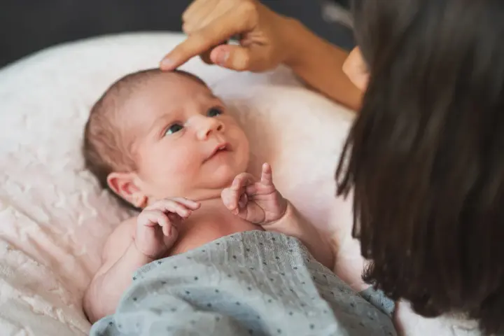 Dłoń rodzica delikatnie dotyka ciemiączka noworodka leżącego na różowej poduszce.