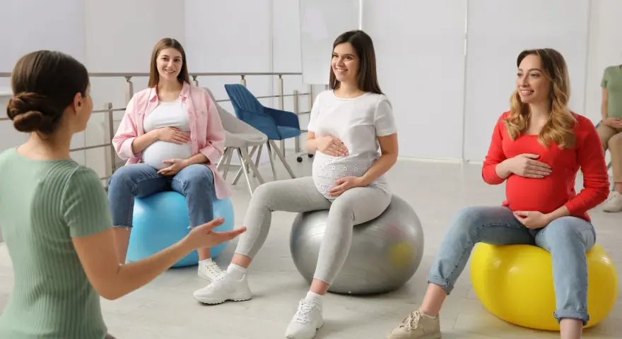Ciężarne kobiety siedzą na piłkach gimnastycznych podczas zajęć w szkole rodzenia.