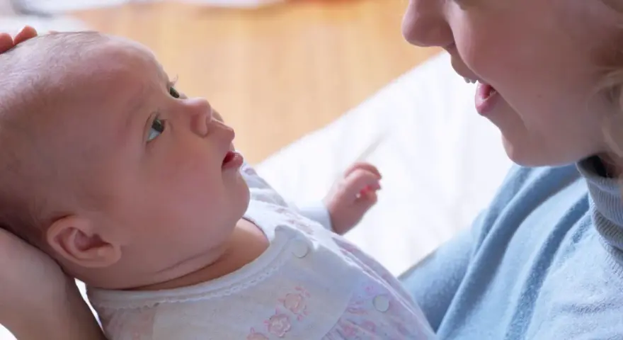 Uśmiechnięta mama patrzy na swoje 6 tygodniowe dziecko, które z zaciekawieniem spogląda w górę.