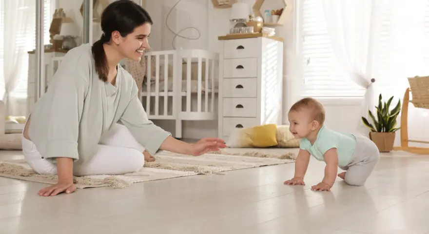 Uśmiechnięta mama zachęca do pierwszych kroków, kiedy dziecko raczkuje po dywanie w pokoju dziecięcym.