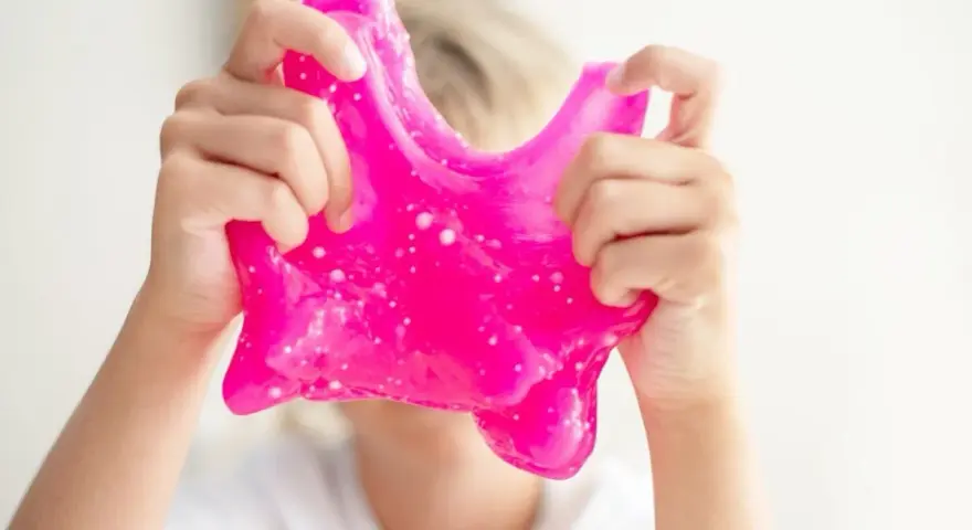 Dziecko bawi się różowym slime, rozciągając go. To świetna zabawa i prosty sposób, jak zrobić slime w domu.