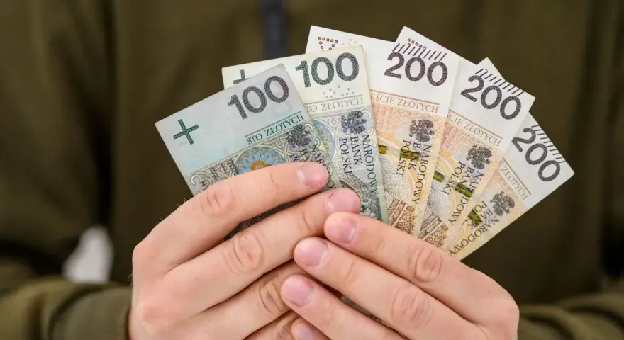Dłonie trzymają polskie banknoty: 100 i 200 zł. To symbol nagrody za pracę, jak 800 plus tylko dla pracujących.
