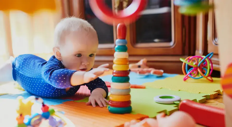 Zaintrygowany 6 miesięczne dziecko próbuje sięgnąć kolorowych kółek wieży.
