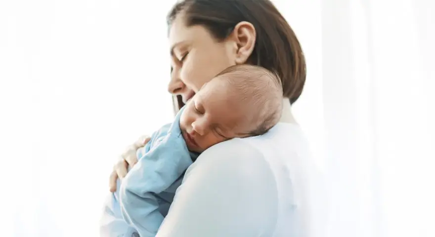 Matka tuląca śpiącego niemowlaka na ramieniu.