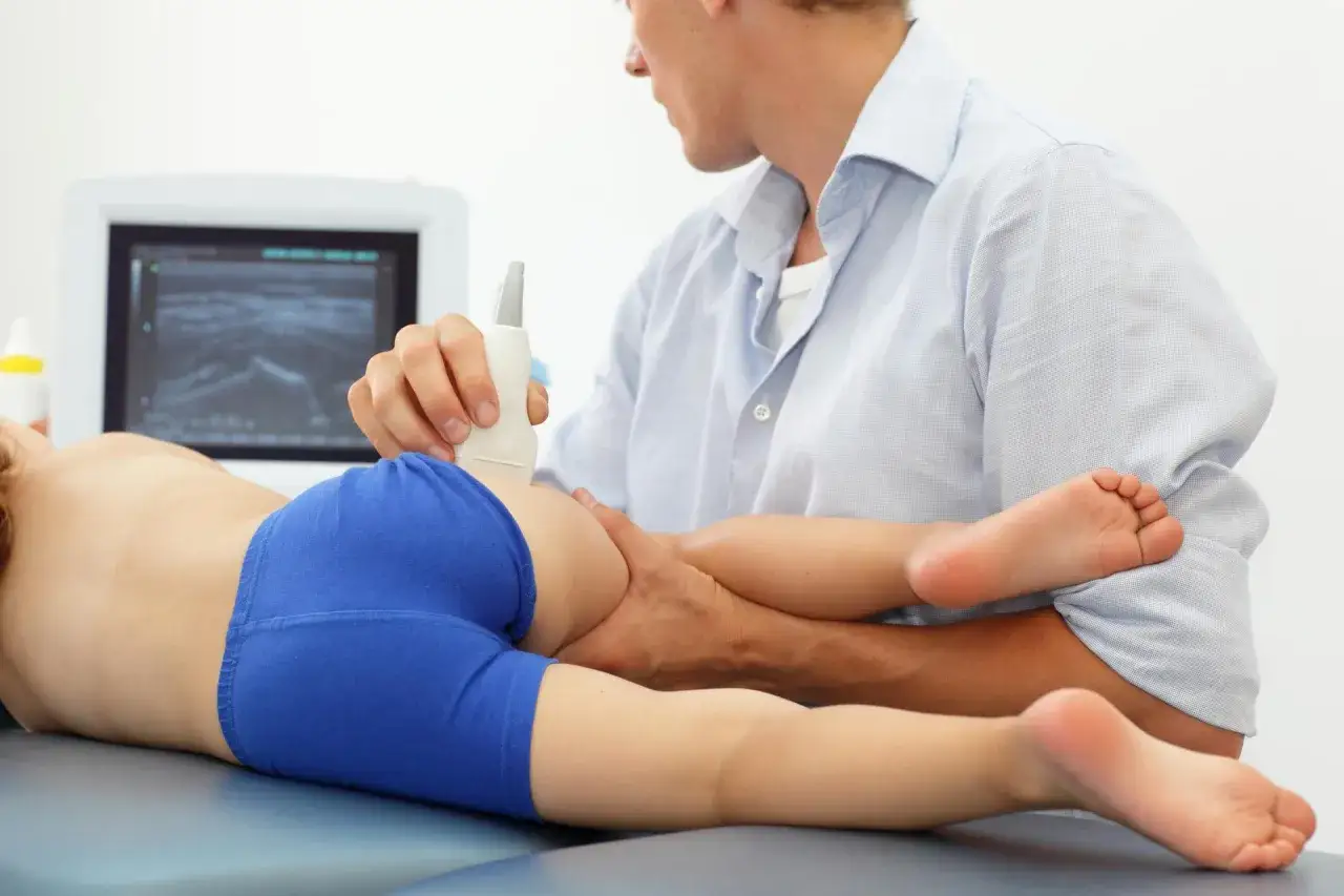 Lekarz wykonuje USG bioder u dziecka, diagnozując zapalenie stawu biodrowego.