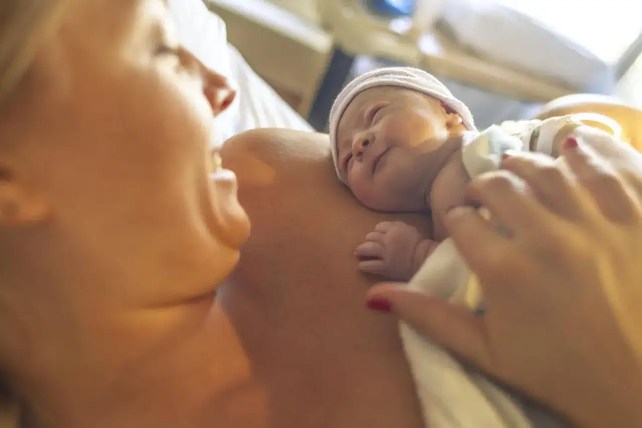 Mama patrzy na swojego nowo narodzonego synka, który śpi wtulony w jej pierś.