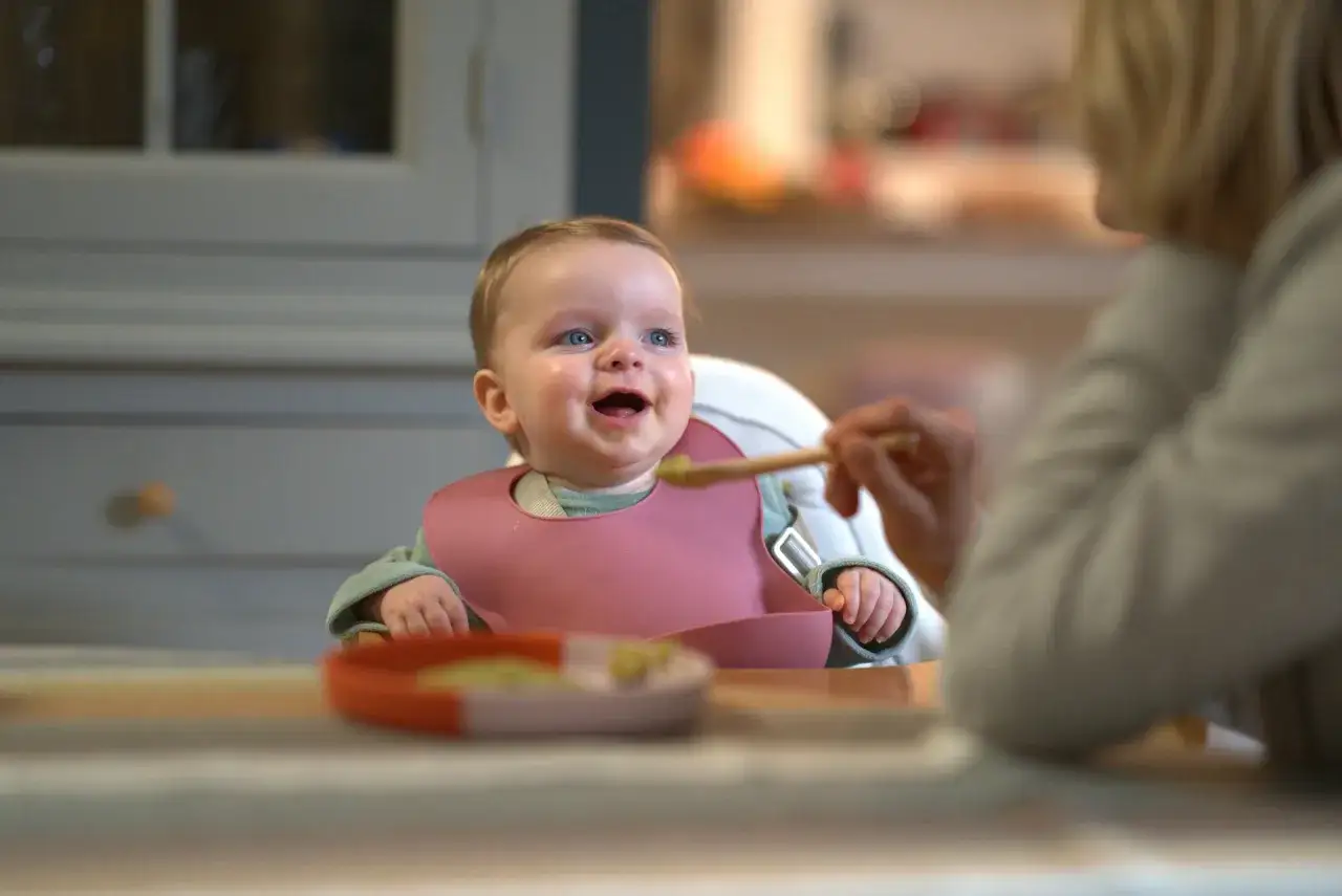 Uśmiechnięty niemowlak w śliniaczku dostaje łyżeczkę z zielonym puree. To pewnie pyszna cukinia dla niemowlaka!