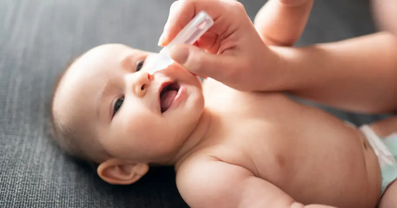Mama zakrapia noskowi dziecka kroplami, by ulżyć mu przy zatkanym nosku. Maluch patrzy z zaciekawieniem.